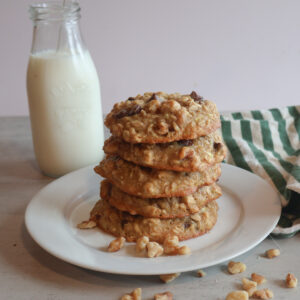 Zucchini breakfast cookies stacked on a white plate with a glass of milk.