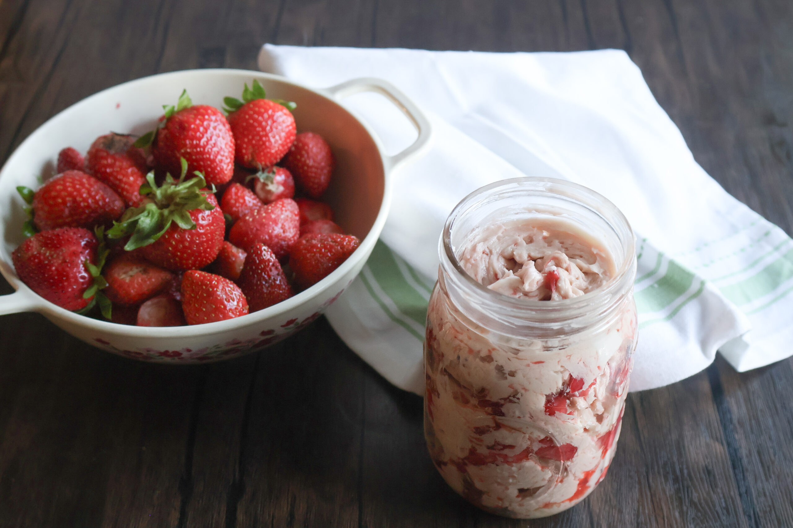 Strawberry butter with a colander of fresh strawberries.