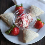 Strawberry butter on a white plate with vanilla scones and strawberries.
