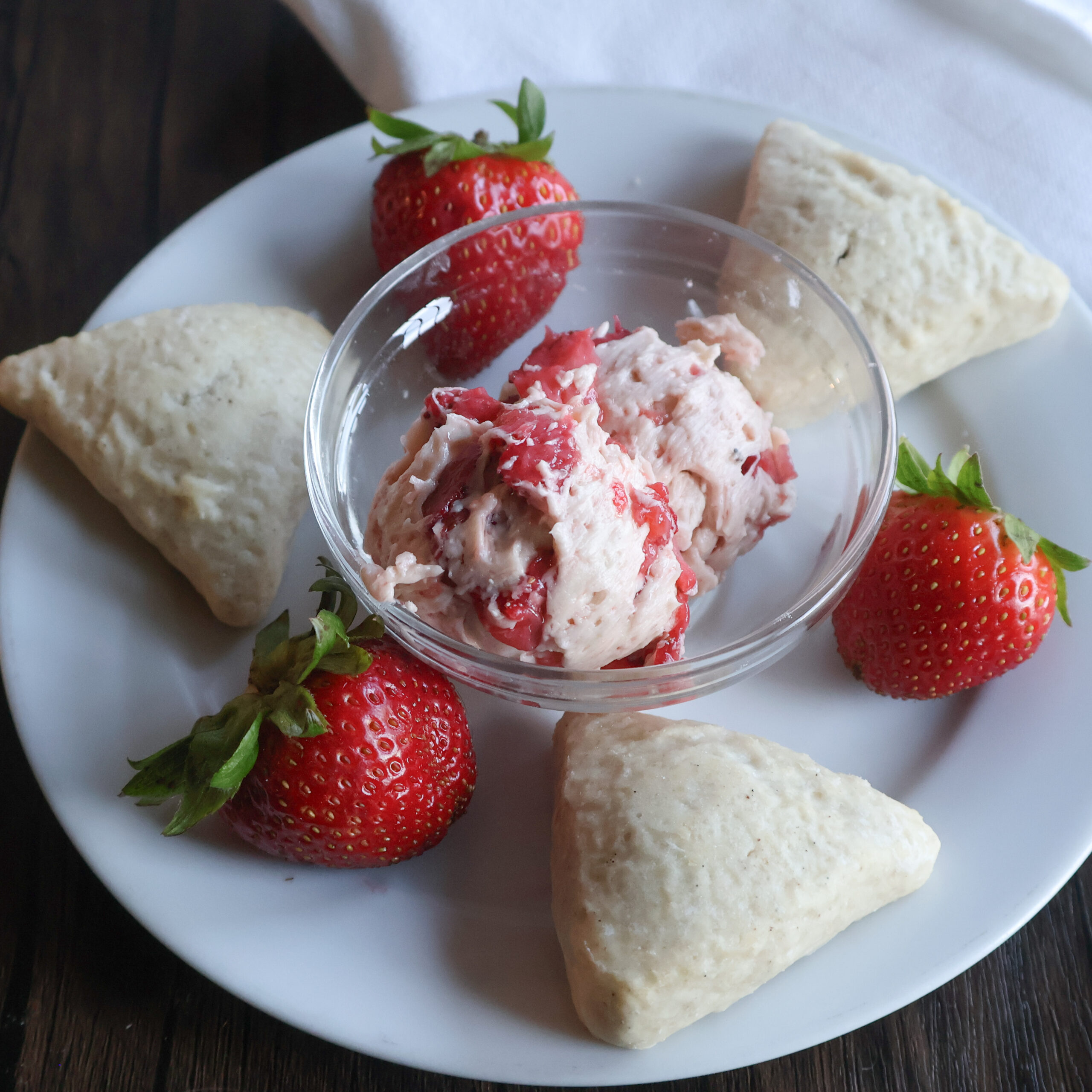 Strawberry butter in a glass dish with scones and strawberries on a white plate.