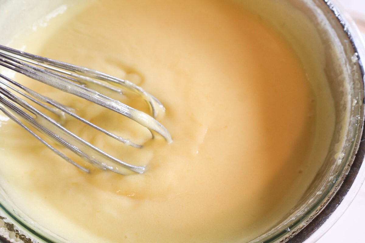 Lemon curd in a glass bowl with a whisk.