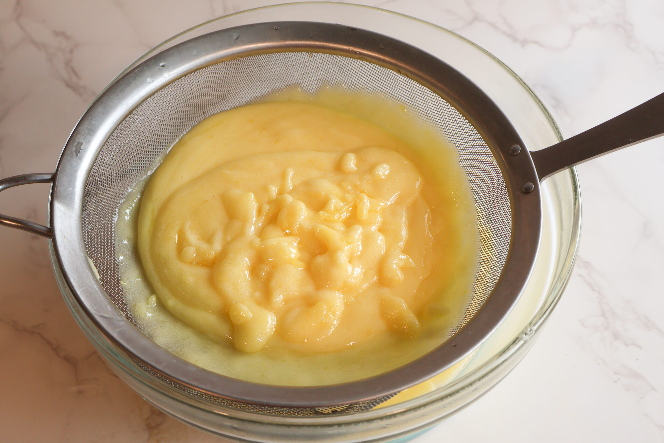 Lemon curd being strained into a glass bowl.