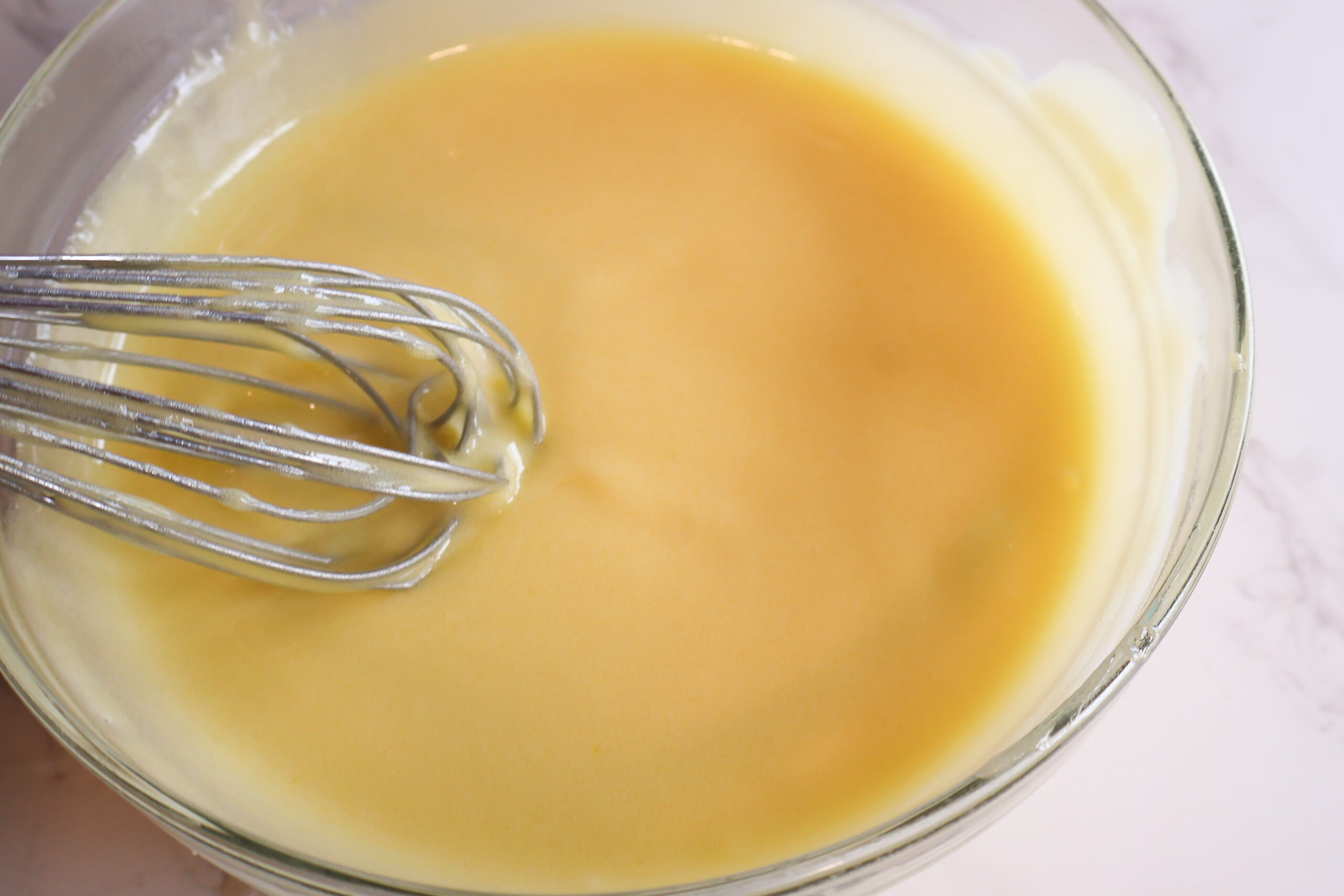 Lemon curd in a glass bowl with a whisk.