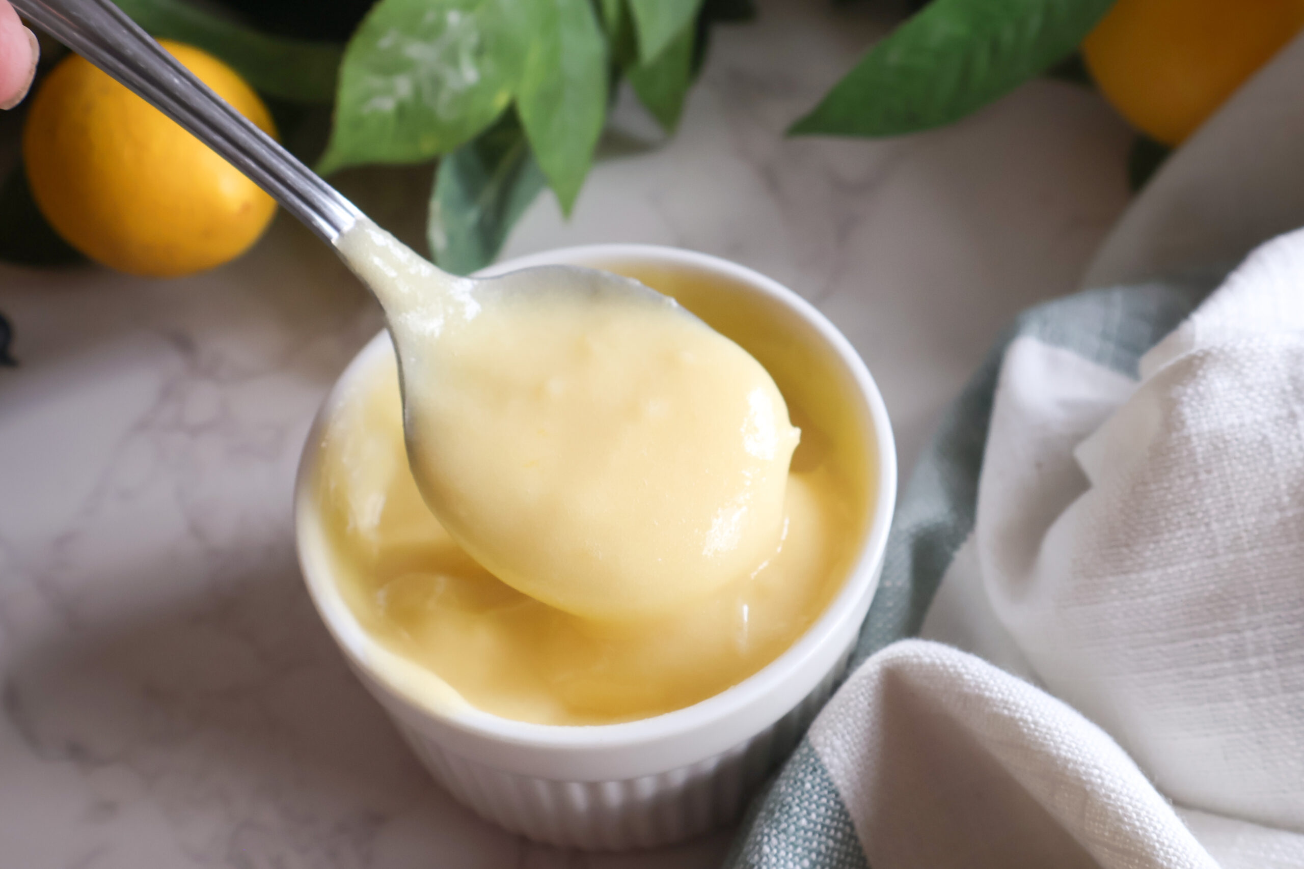 Lemon curd in a small white dish with a spoon.