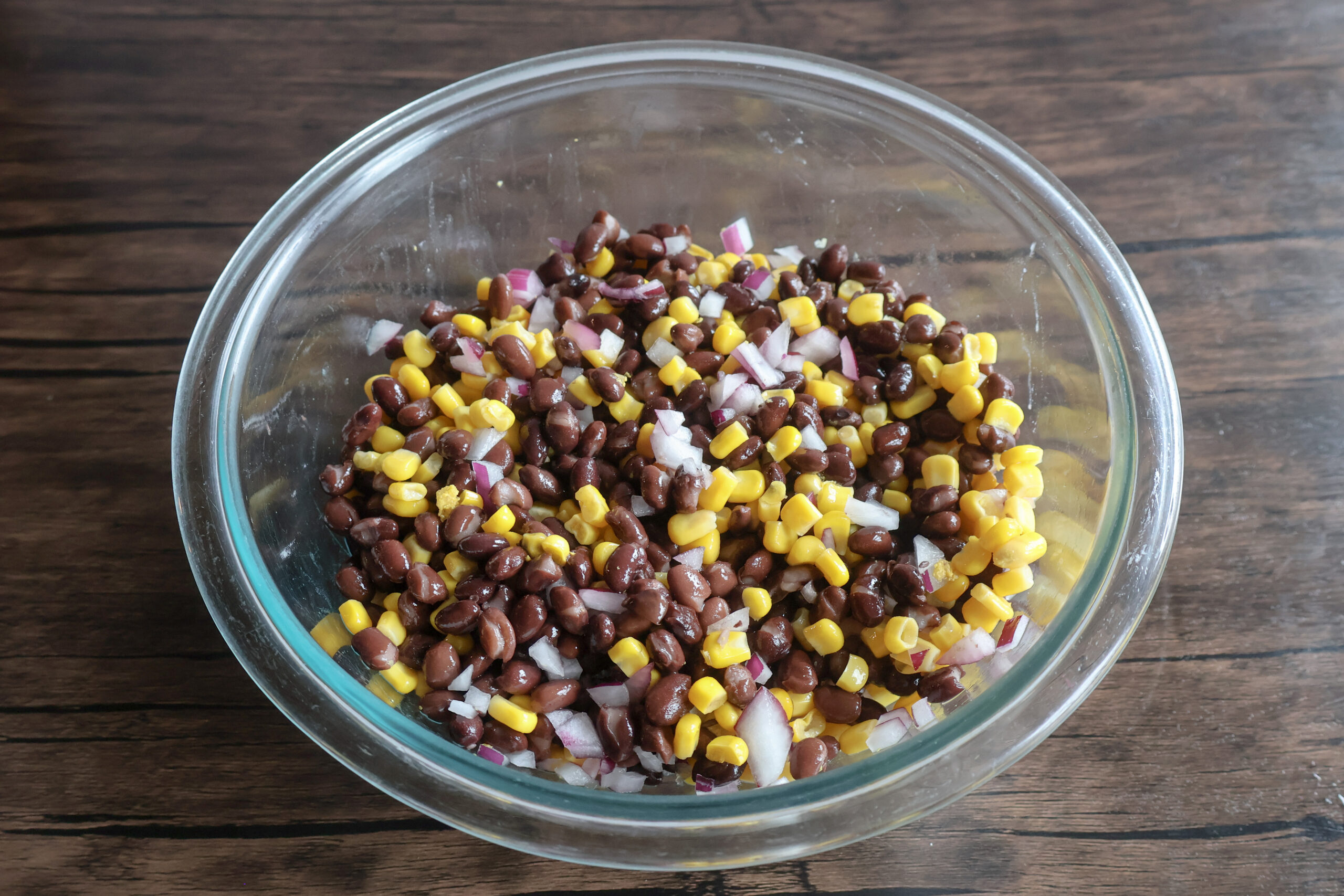 Black beans, corn, and red onion mixed in a glass bowl.