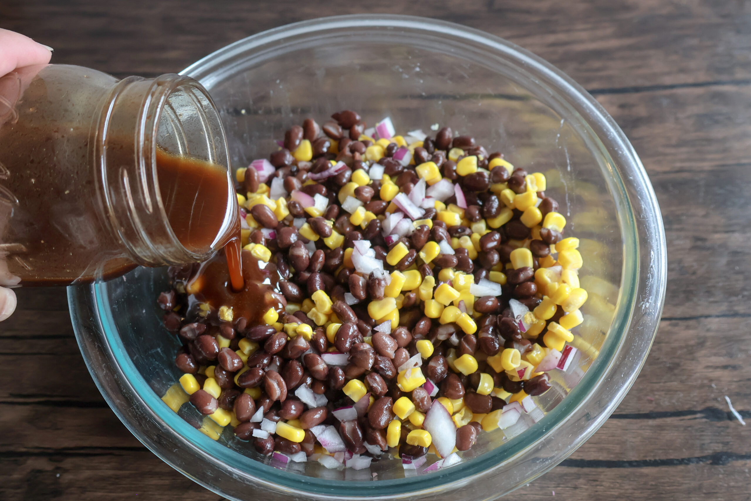 sauce being poured over the black bean and corn dip.