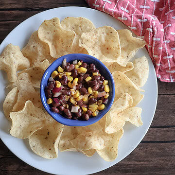 Black bean and corn dip in a small ramekin on a white plate with chips.
