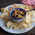 corn and black bean dip on a white plate with tortilla chips.