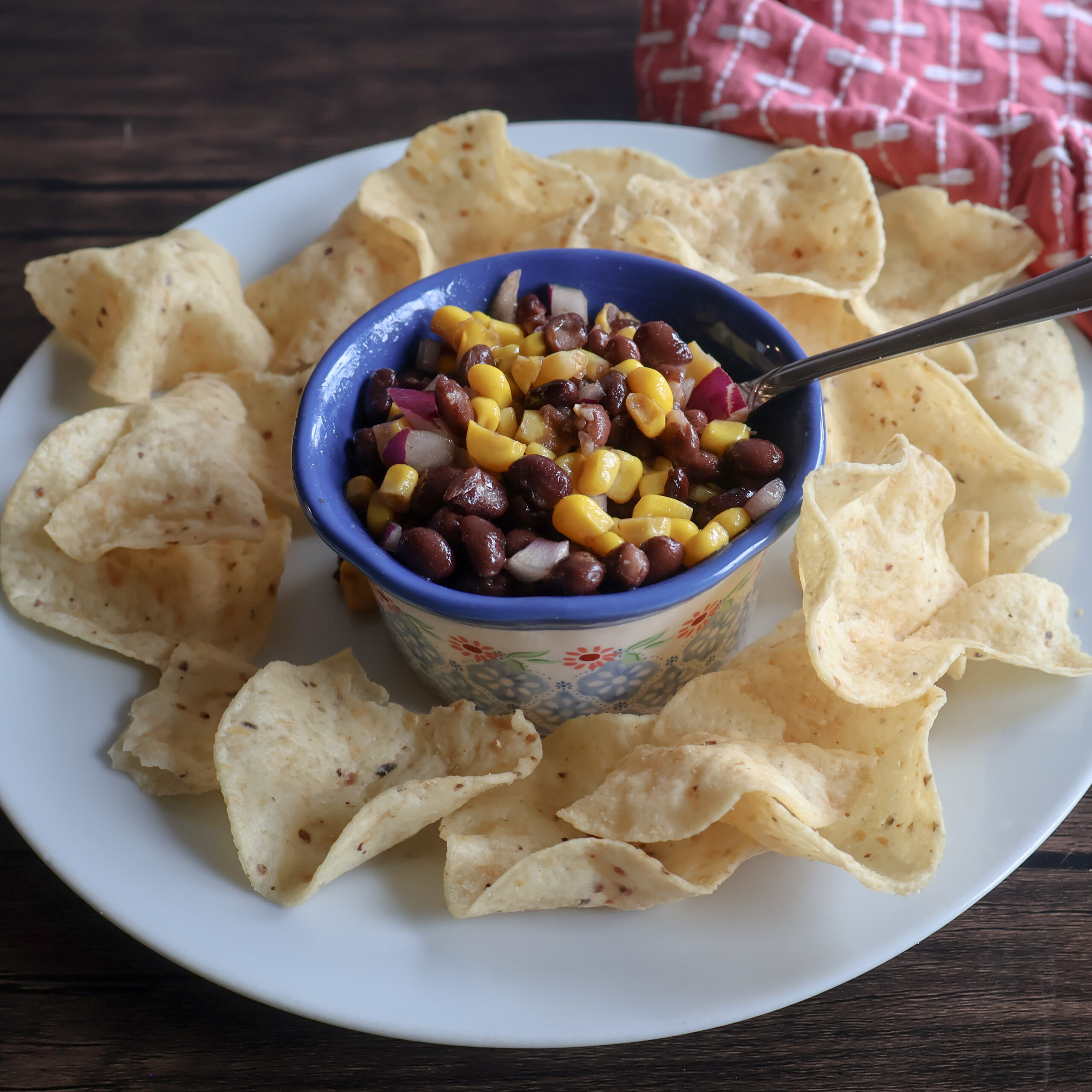 Black bean and corn dip in a blue ramekin with a spoon on a white plate with chips.