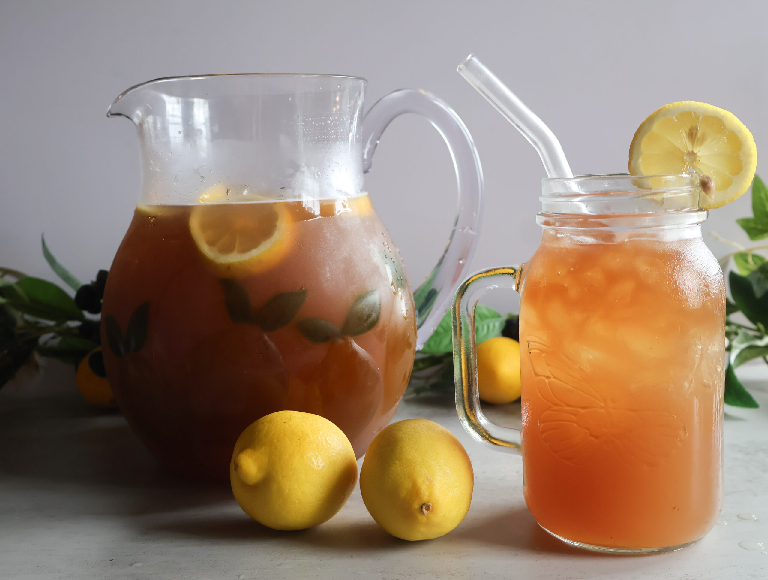 Summertime cooler in a glass pitcher and a mason jar glass with a straw anf a lemon slice.