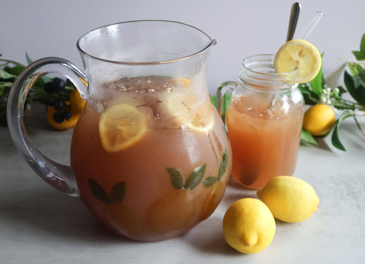 Summertime cooler in a clear pitcher with a glass and lemons.