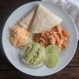 crockpot chicken tacos with cheese and sliced lime on a white plate.