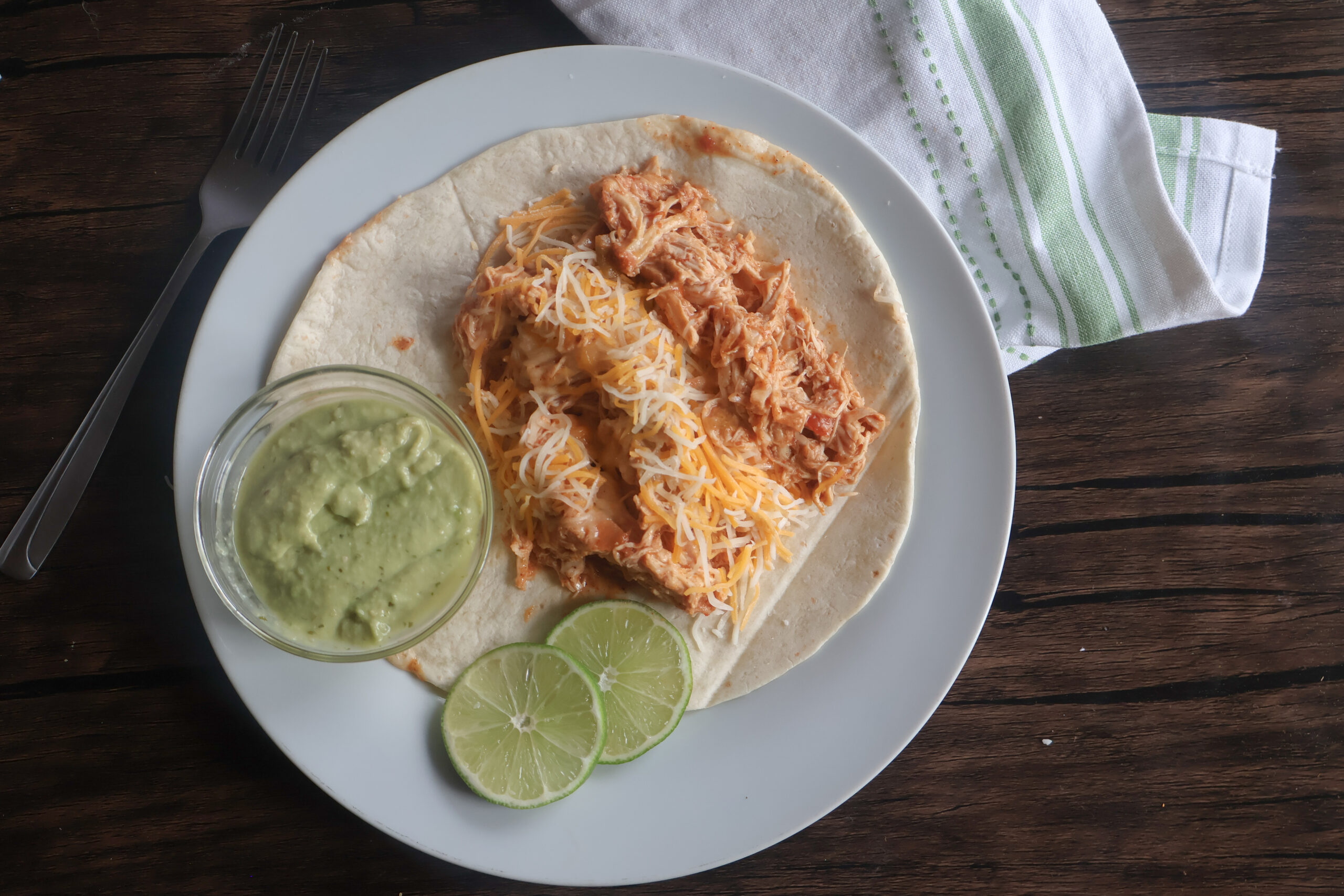 Crockpot chicken tacos on a white plate with lime slices.