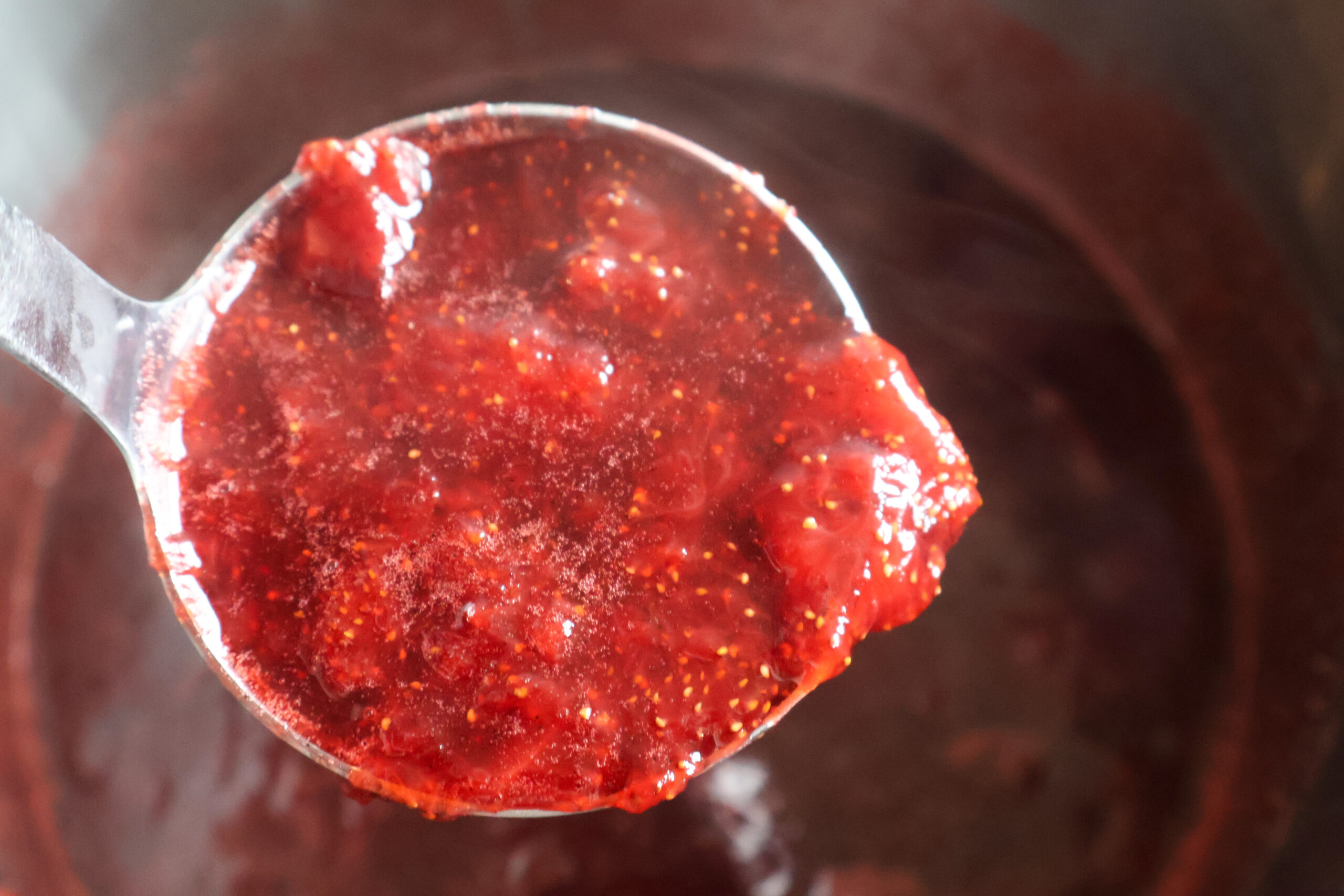 Ladle full of honey strawberry preserves.