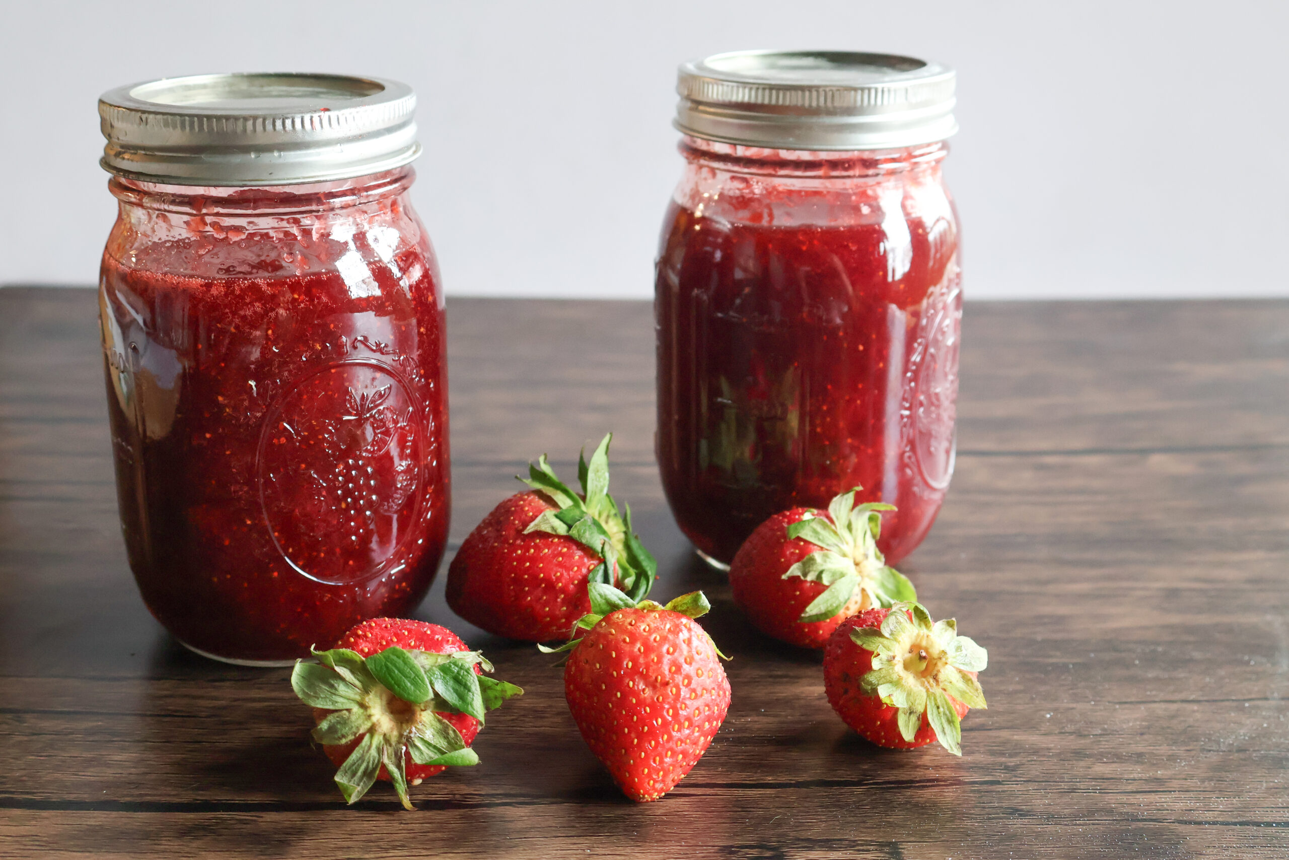 Homemade honey strawberry preserves in a jar with fresh strawberries.