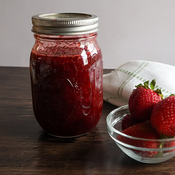 honey strawberry preserves in a mason jar with a small bowl of strawberries.