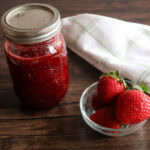 Strawberry honey preserves in a jar with a bowl of strawberries.