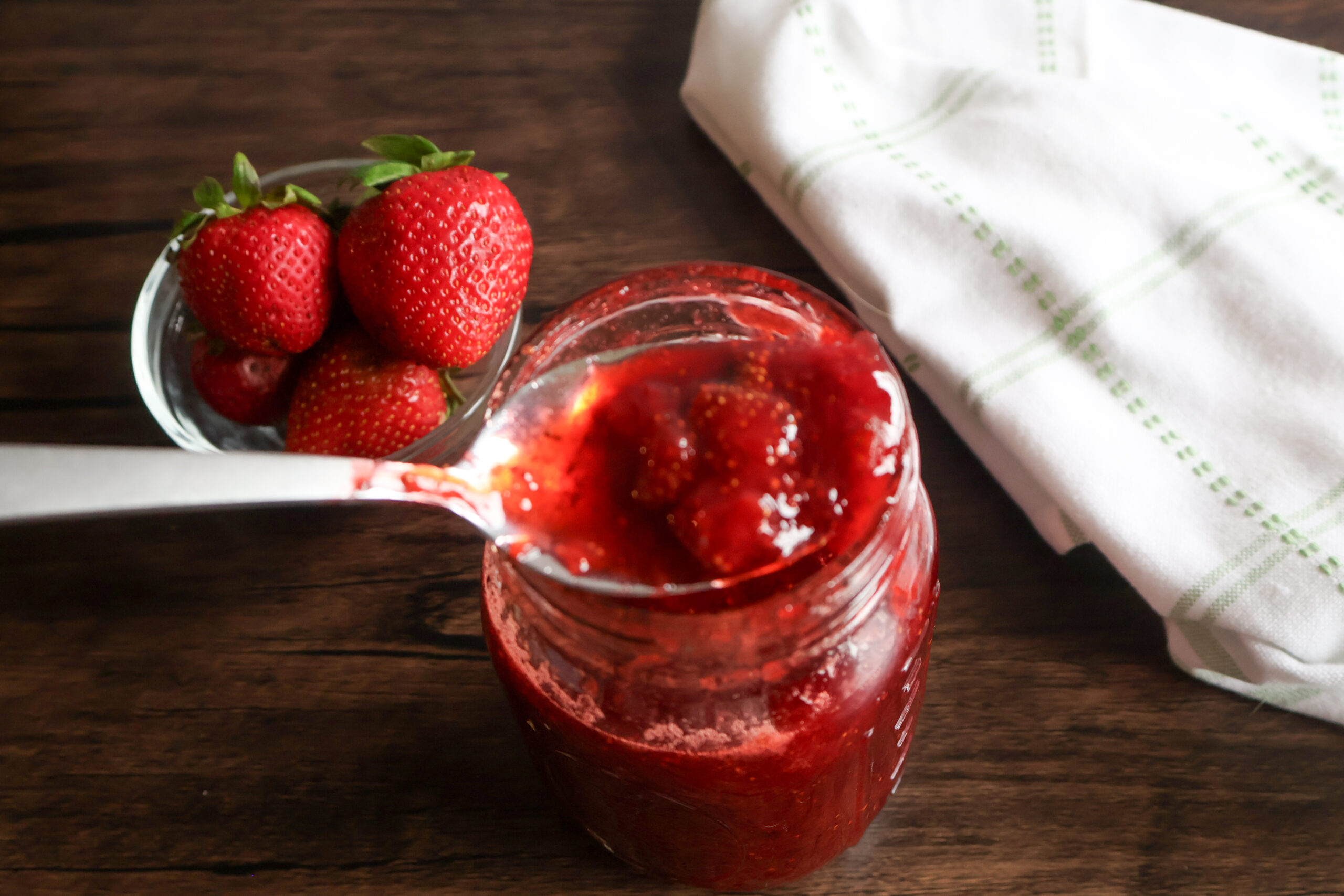 spoonful of honey strawberry preserves with a small dish of strawberries and a tea towel.