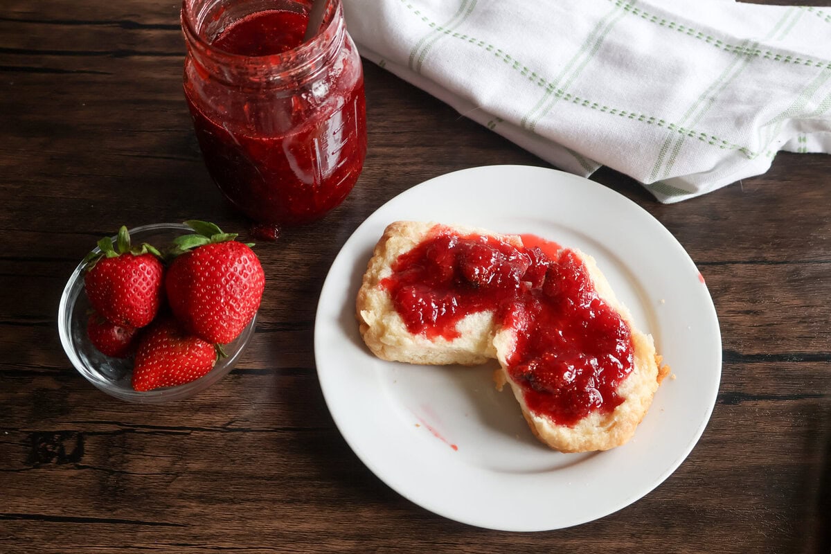 Homemade Strawberry Honey Preserves on a biscuit, and a bowl of fresh strawberries.
