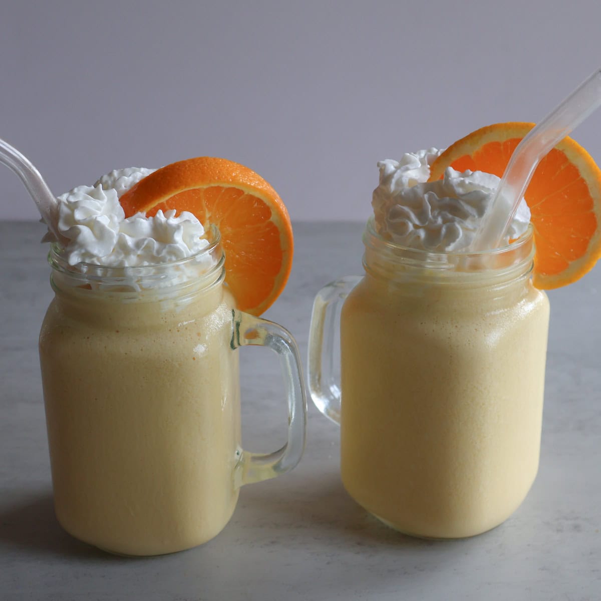 Creamsicle orange frost in mason jar glasses with whipped cream and orange slices.