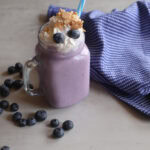 Blueberry Cheesecake Milkshake in a glass with fresh blueberries and a tea towel.