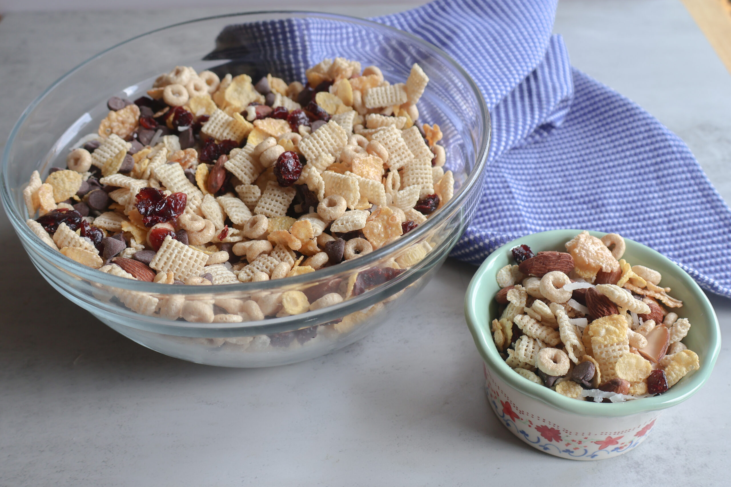 Easy Homemade Cereal Trail Mix in a large and small bowl with a blue ea towel.