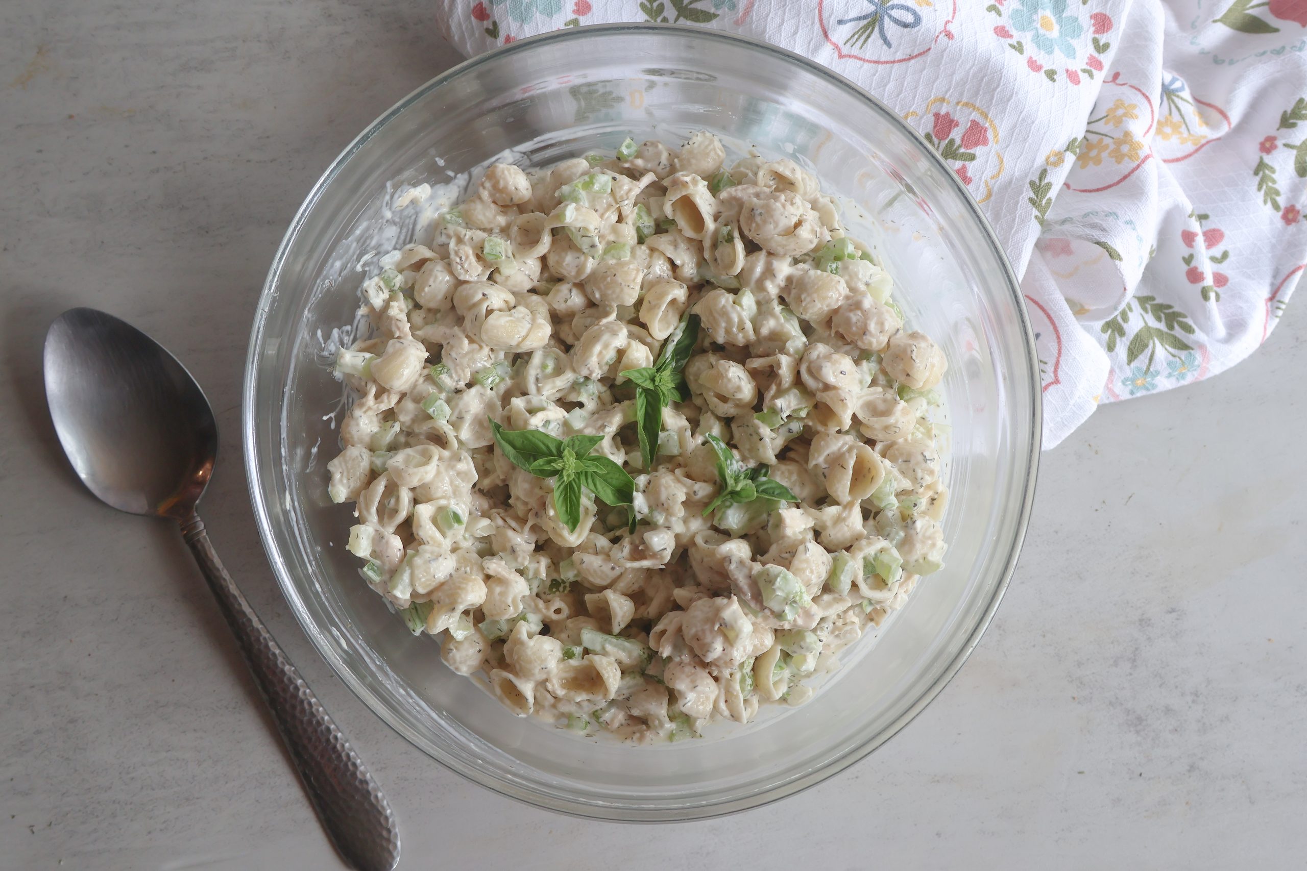 Creamy Tuna Pasta Salad in a glass bowl with a spoon and tea towel.