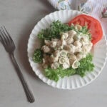 Creamy Tuna Pasta Salad on a white plate with lettuce and tomato and a fork.