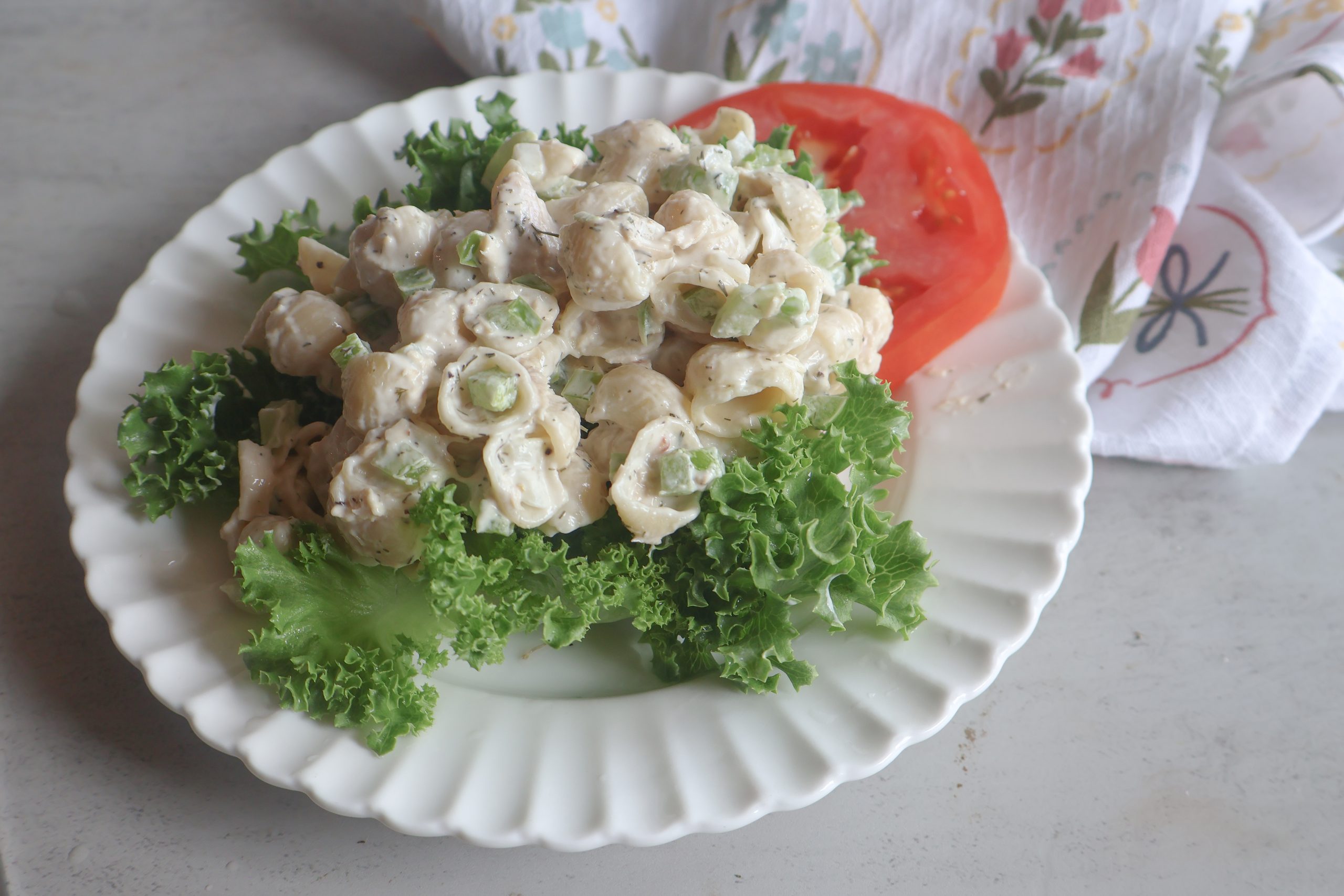 Creamy Tuna Pasta Salad on a white plate with lettuce and a tomato slice.