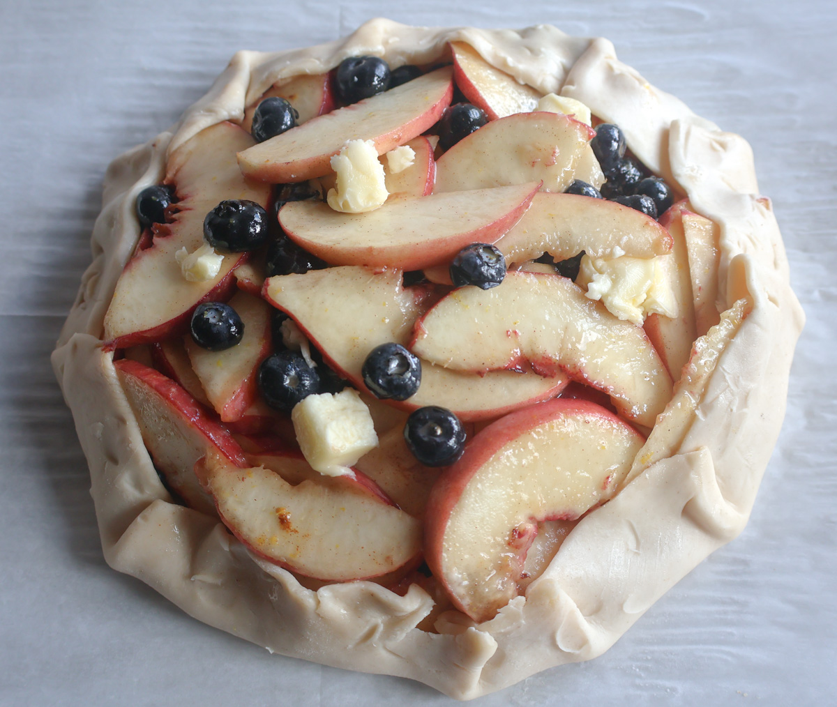 Blueberry peach galette with the crust folded over with small pieces of butter.