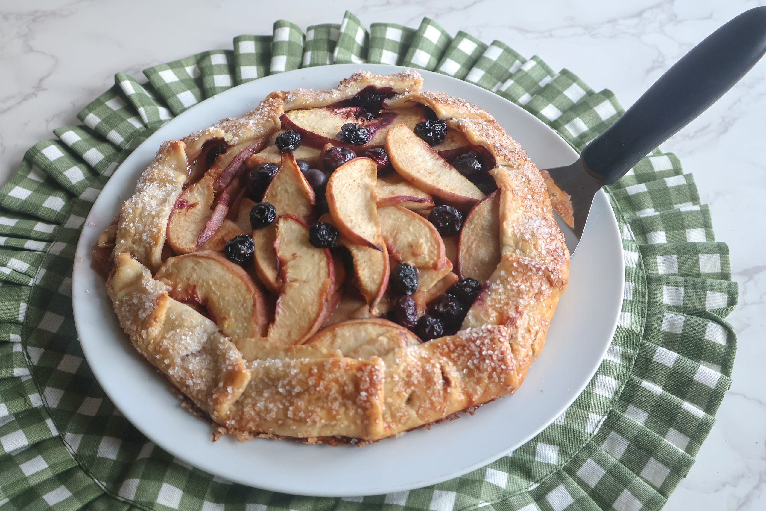Blueberry Peach Galette on a white plate with a green and white placemat and a serving spatula.