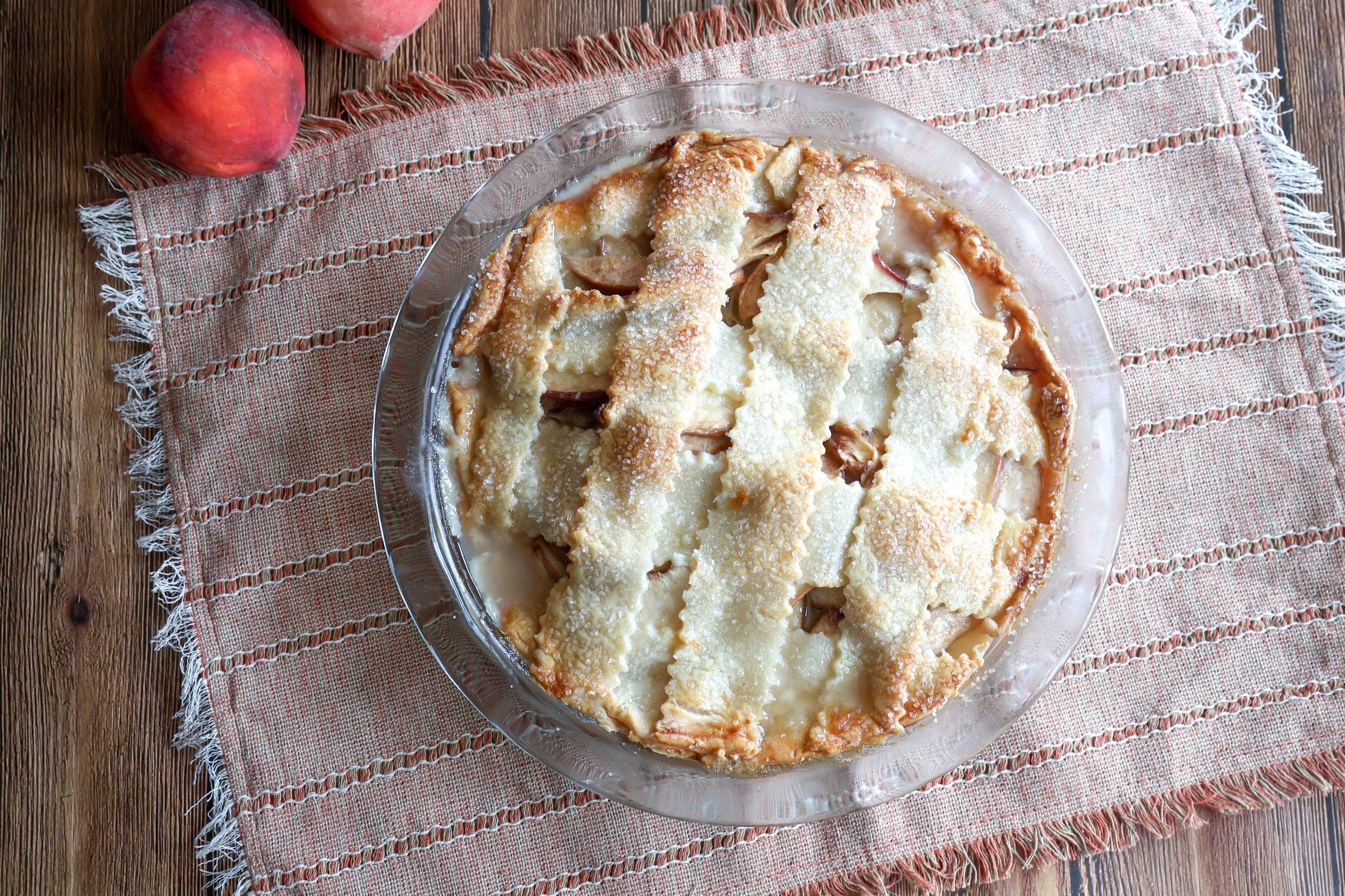 Fresh peach custard pie on a tan placemat with fresh peaches.