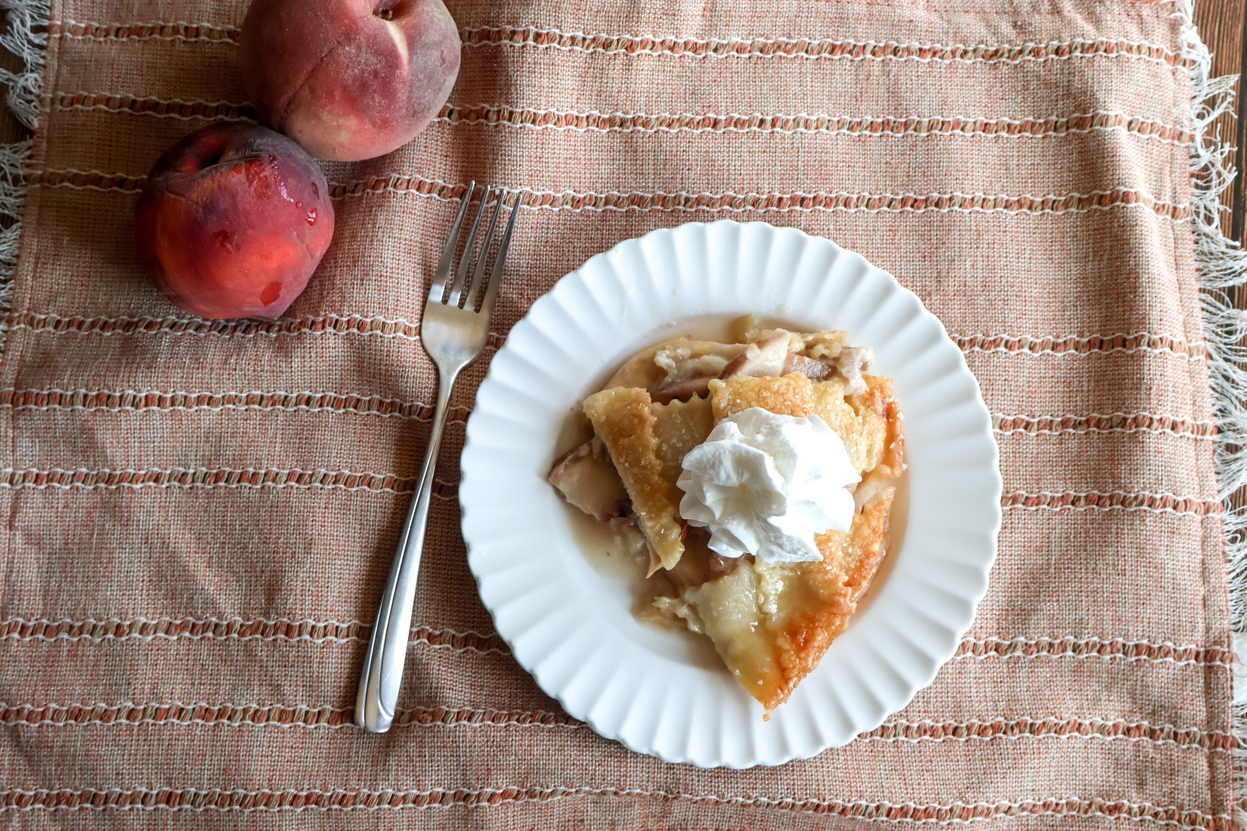 One slice of fresh peach custard pie with a fork annd peaches.