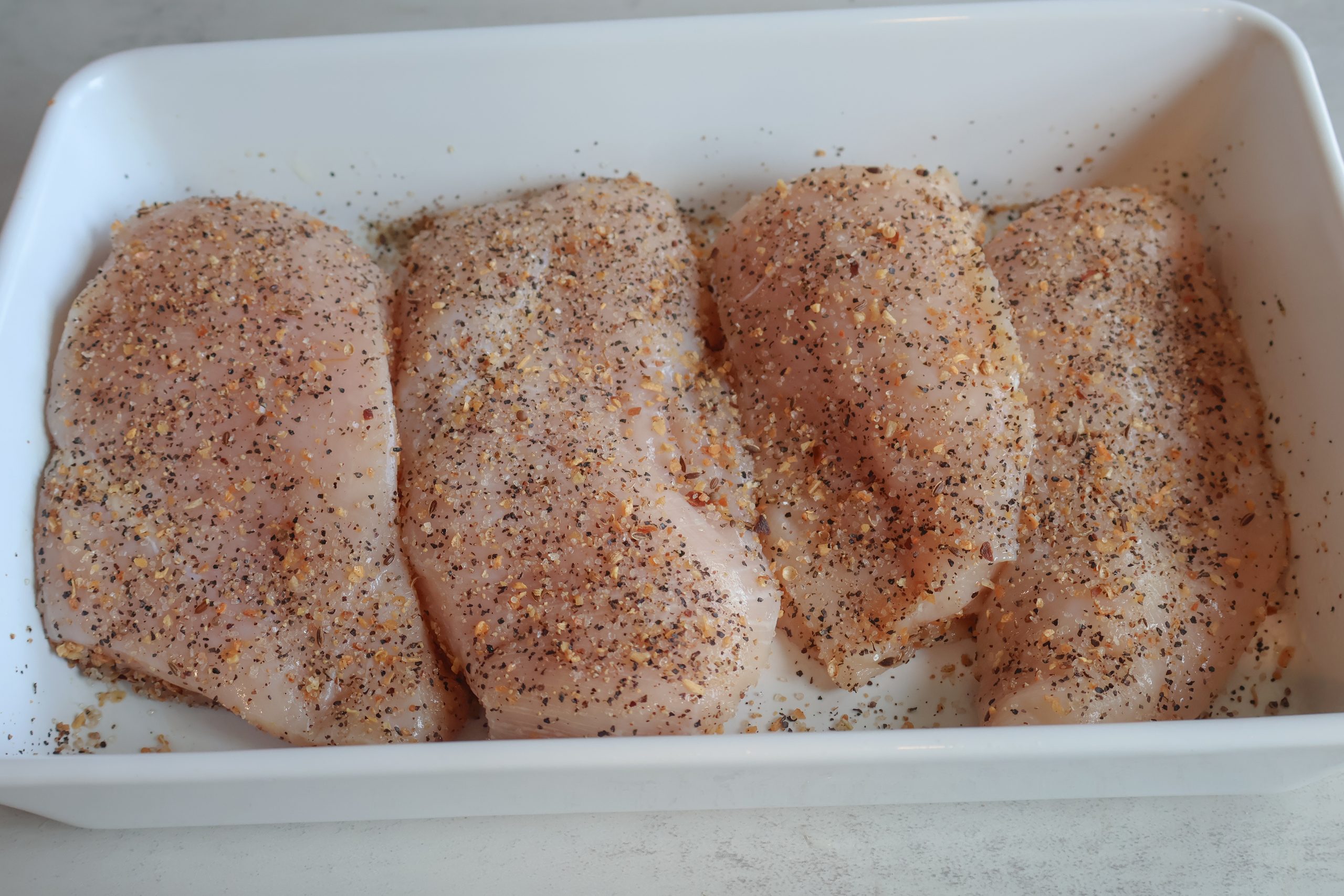 Seasoned Vidalia almond chicken in a white baking dish.