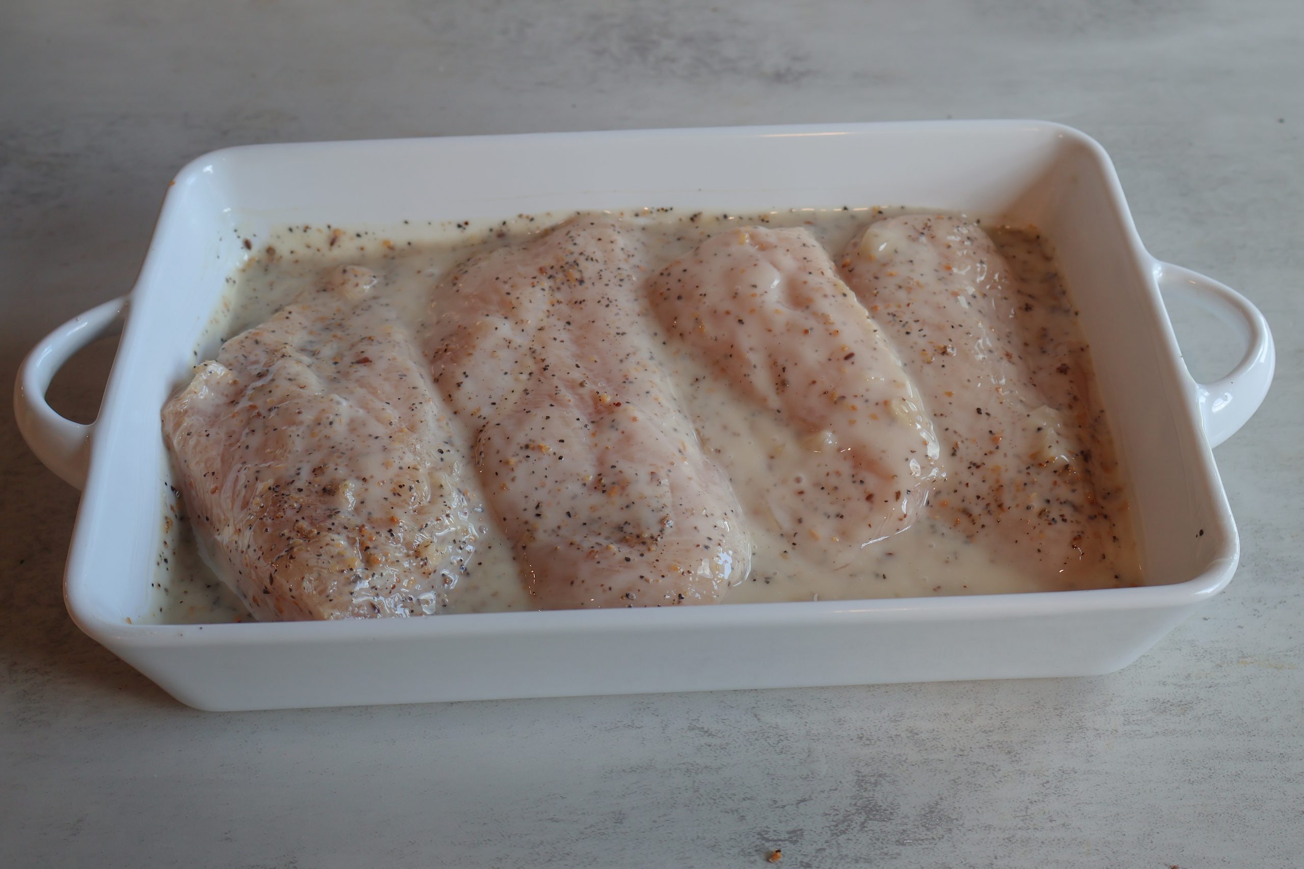 Vidalia onion almond chicken with sauce in a white baking dish.