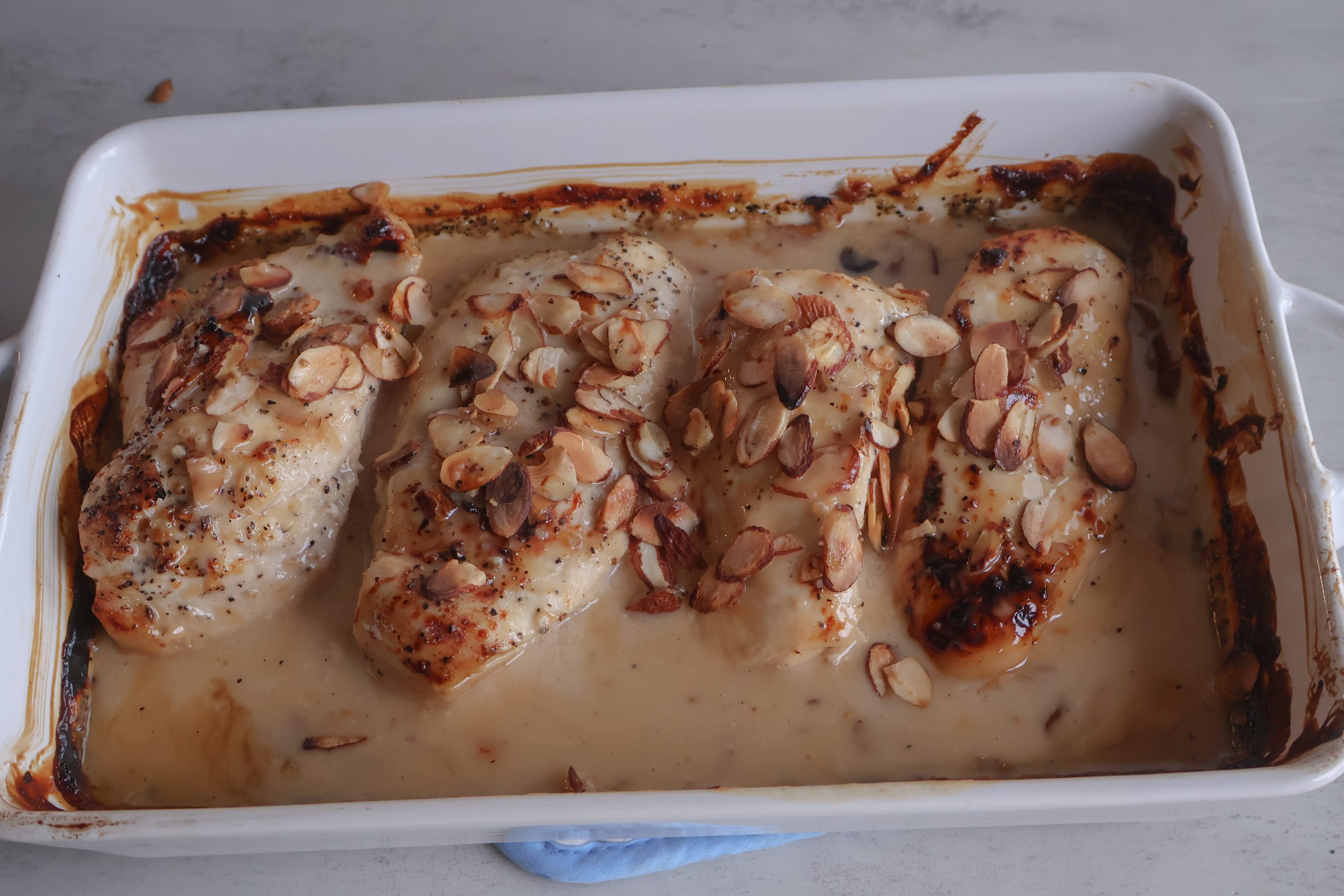 Broiled vidalia onion almond chicken in a white baking dish.