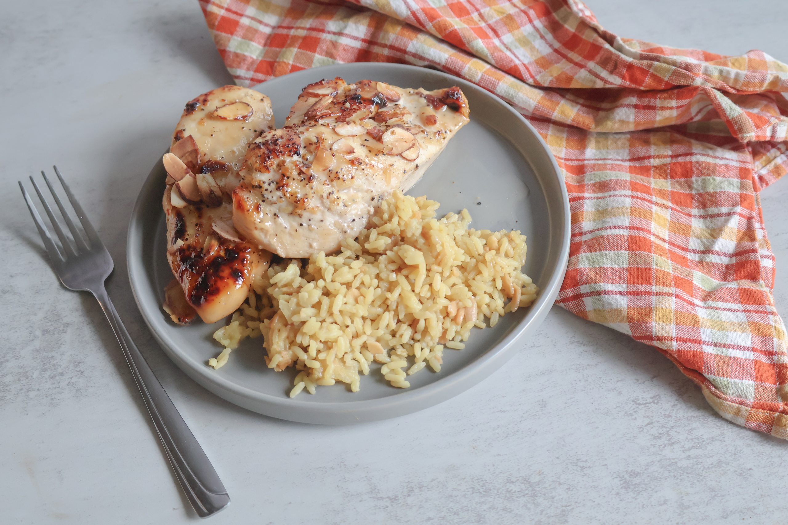 Vidalia onion almond chicken on a gray plate with rice, a fork and orange tea towel.