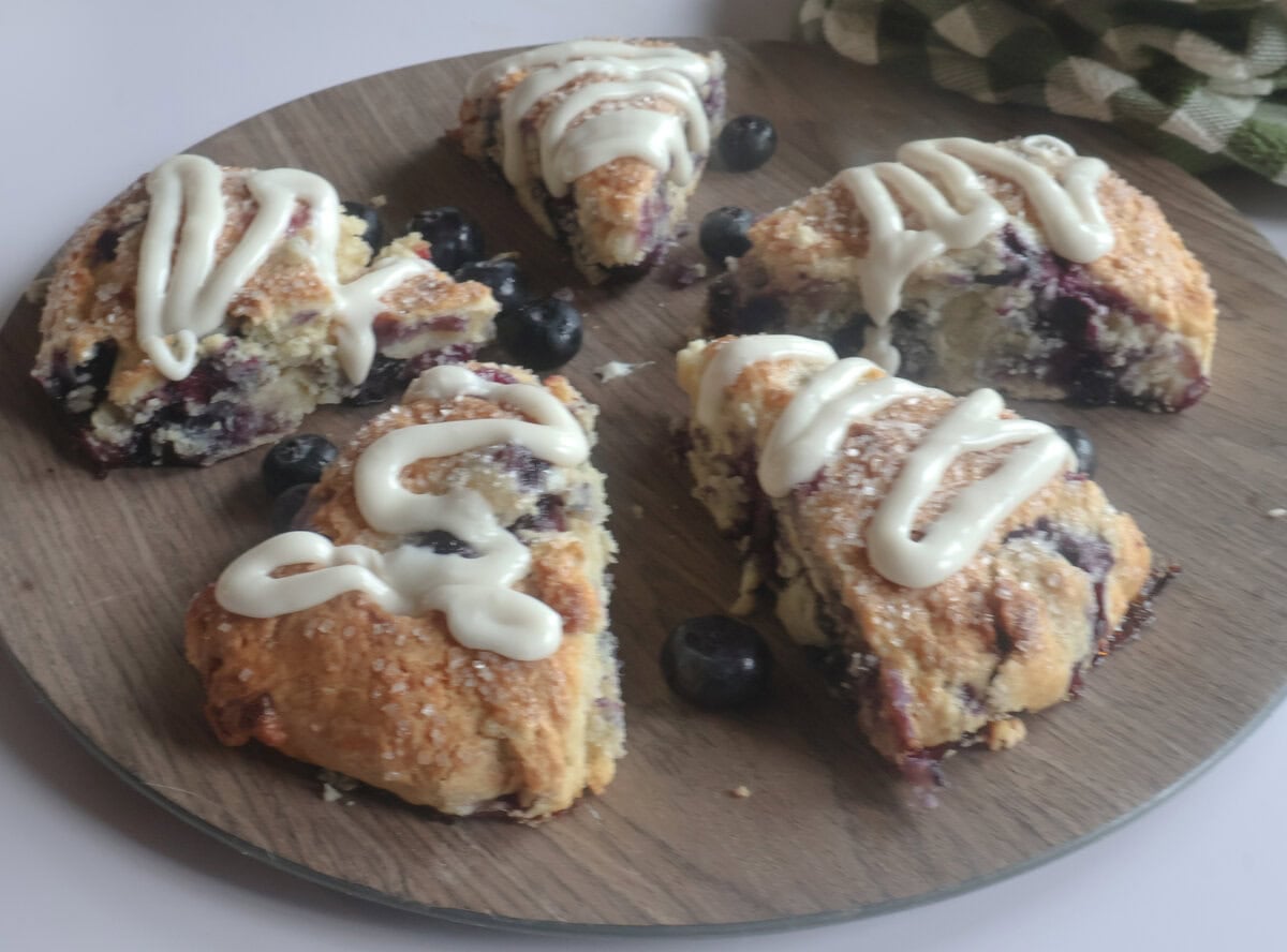 blueberry white chocolate scones glazed on a brown plate with fresh blueberries.