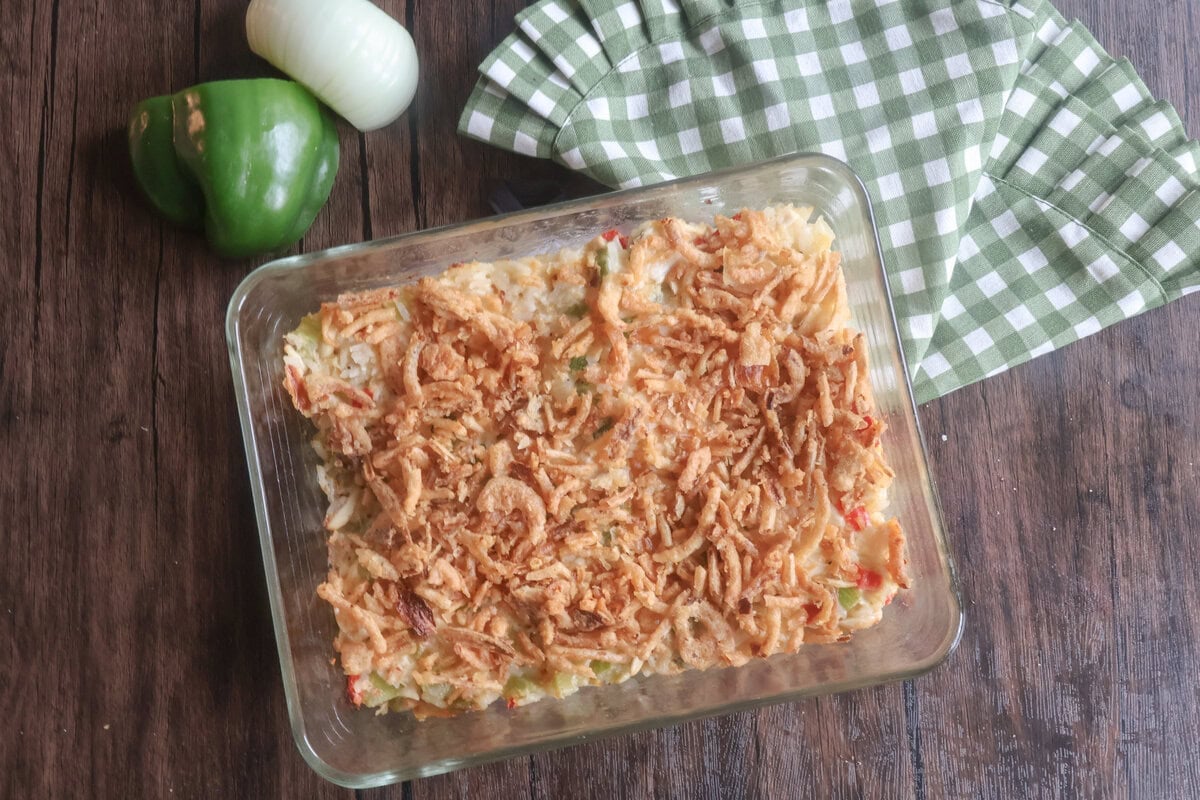 baked chicken salad with rice in a casserole dish with a pepper and onion and green and white checkered napkin.