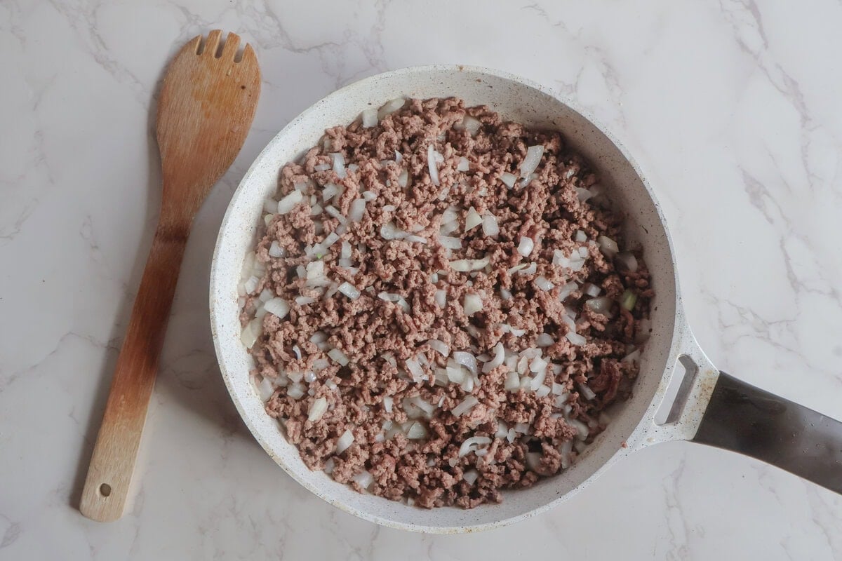 ground beef and onion cooked in a pan with a wooden spoon.