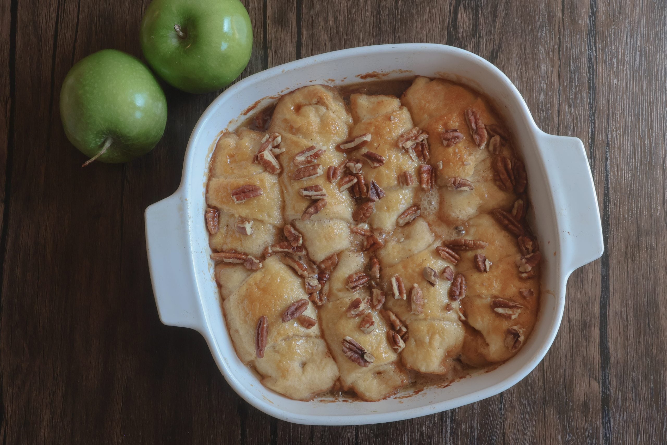 baked caramel apple dumplings in a white dish with 2 apples.
