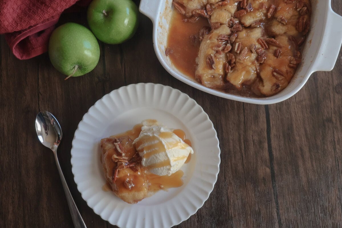 easy caramel apple dumplings in a white casserole dish with fresh apples and on a white plate with a spoon.