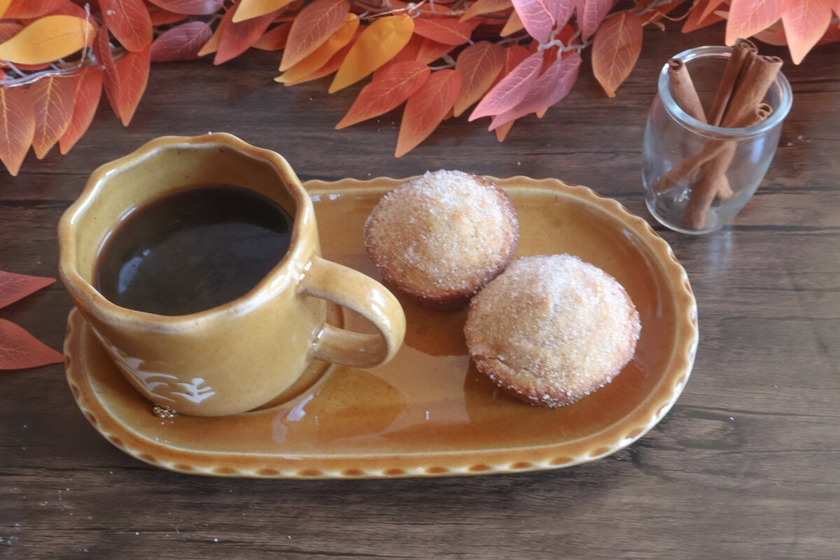 Apple cider donut muffins on a tan plate with a cup of coffee.