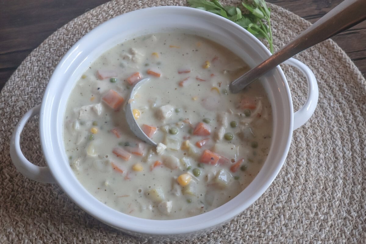 creamy chicken pot pie soup with a ladle in a white crock.