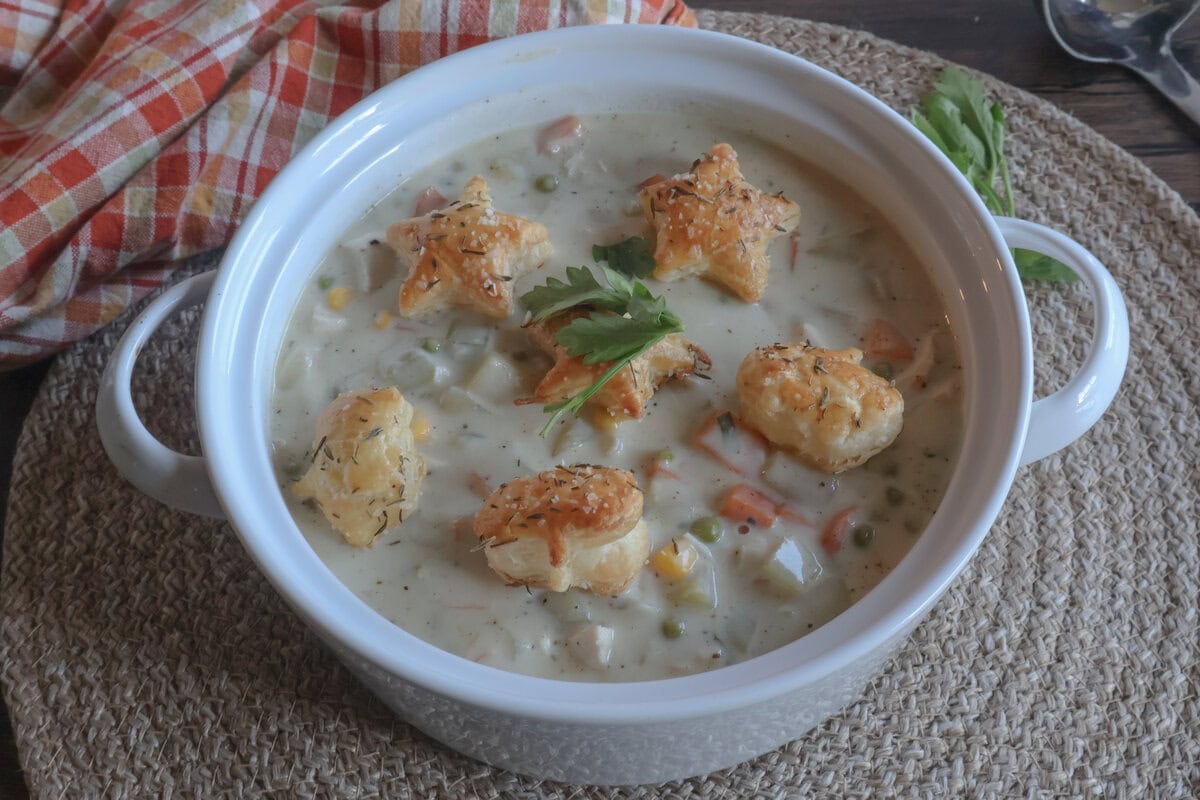 creamy chicken pot pie soup with puff pastry croutons in a white bowl on a brown placemat.