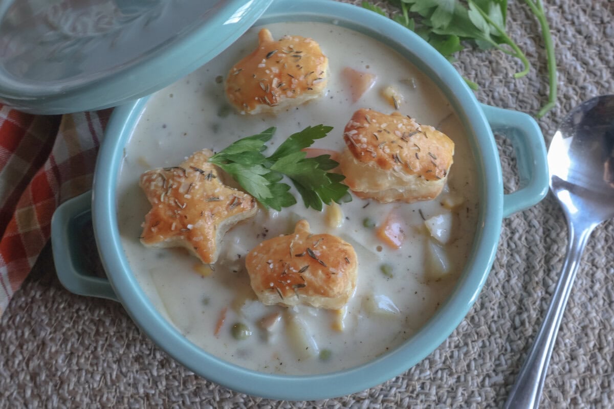 creamy chicken pot pie soup in a blue crock with puff pastry croutons.