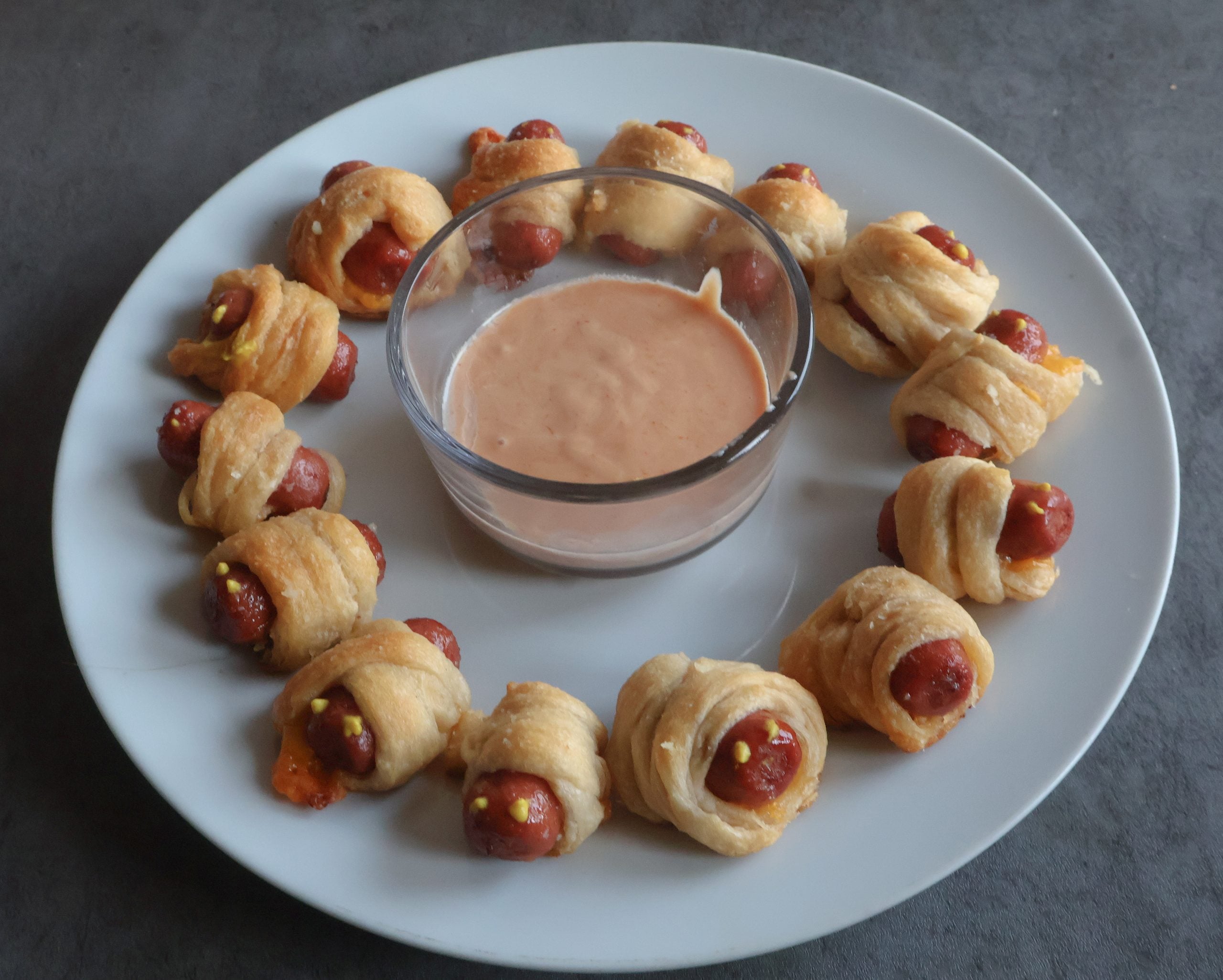 mini mummy hot dogs on a white plate with dipping sauce.