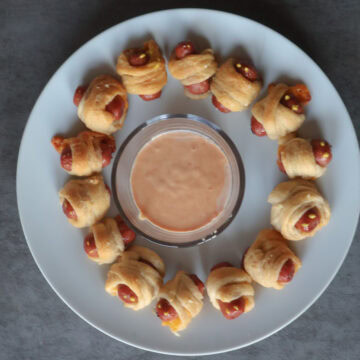 mini mummy hot dogs on a white plate with dipping sauce.