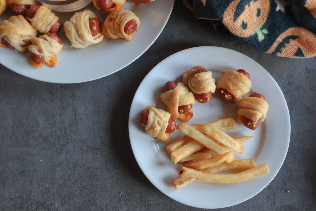 mini mummy hot dogs on a platter and a small plate with fries.
